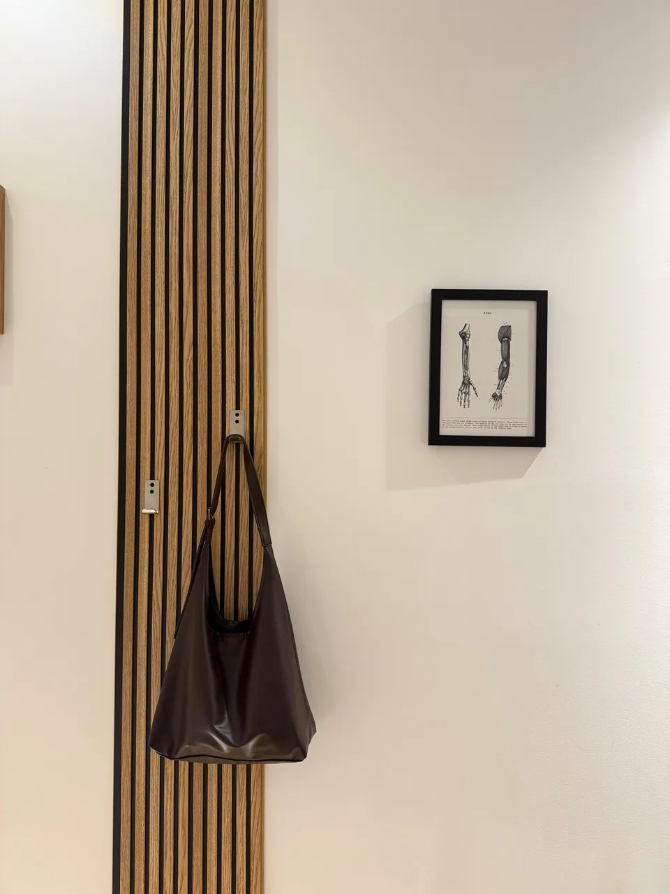 Wooden slat wall panel with a hanging bag and a framed anatomy print